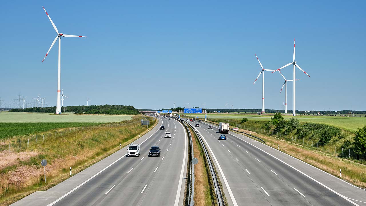 Foto einer Autobahn in Europa mit Windkraftanlagen im Hintergrund.
